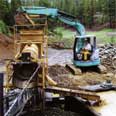 Using a small excavator to load the gold-bearing ore into the trommel.